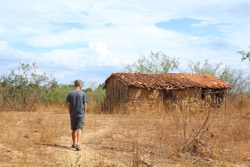 homem caminhando ao lado de casa de taipa abandonada no sertão, interior da bahia 
