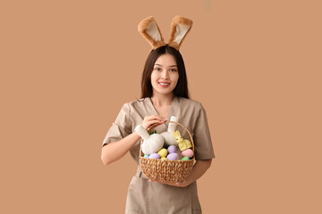 Female Asian massage therapist in bunny ears with Easter eggs and herbal bags on brown background