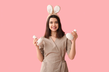 Female massage therapist in bunny ears with herbal bags on pink background. Easter celebration