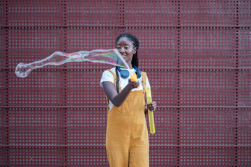 Young woman blowing giant soap bubbles outdoors wearing yellow dungarees.