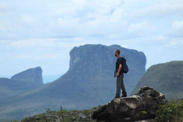 homem de mochila nas costas em trilha na Chapada Diamantina, Bahia, com motanhas ao fundo