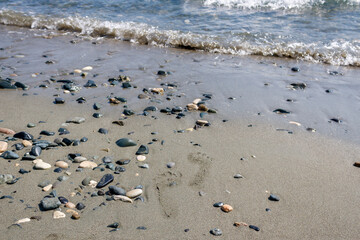 Fototapeta na wymiar Sea beach with two footprints on the sand among stones and pebbles
