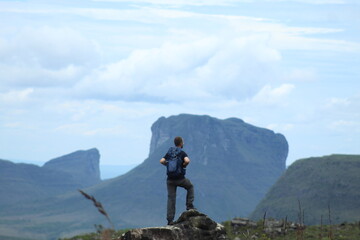 homem de mochila nas costas em trilha na Chapada Diamantina, Bahia, com motanhas ao fundo