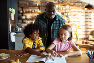 Grandfather helping grandchildren with homework at the kitchen table
