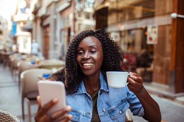 Smiling young woman sitting in city cafe with smartphone