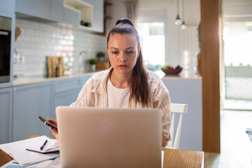 Young woman working on laptop at home kitchen table