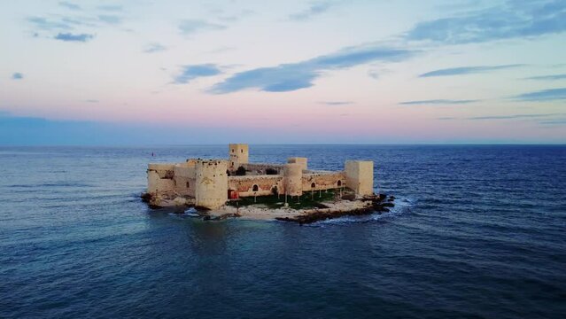 Witness Kizkalesi's ancient allure in breathtaking aerial footage Marvel at colossal ruins of Byzantine castle on Mersin's Mediterranean coast at sunset Uncover the island's rich historical tapestry