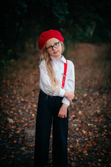 Little blonde girl in glasses, red beret and suspenders in nature