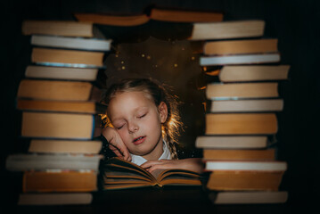 The girl fell asleep reading a book against the background of a stack of books
