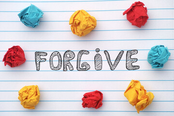 Forgive. The word Forgive written on a notebook sheet with some colorful crumpled paper balls...