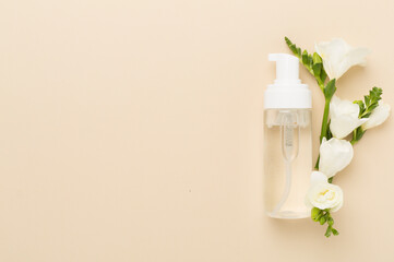 Cosmetic bottle with freesia flowers on color background, top view