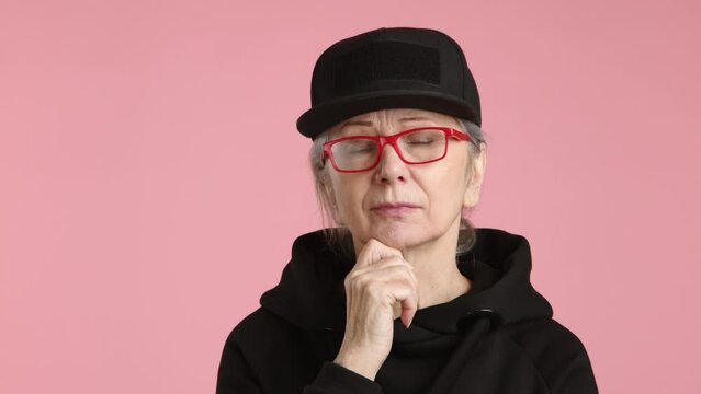 An elderly woman wearing glasses and a black hat contemplates with her eyewear, thinking about vision care and potentially adjusting her sleeve.