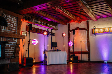 Valmiera, Latvia - July 7, 2023 - Rustic wedding venue interior with purple lighting, DJ booth, and...