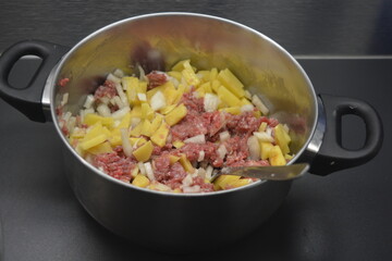 Cooking a delicious and healthy meal, minced meat with onions and sliced potatoes is located in a large metal pot.