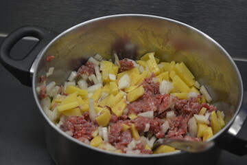 Cooking a delicious and healthy meal, minced meat with onions and sliced potatoes is located in a large metal pot.