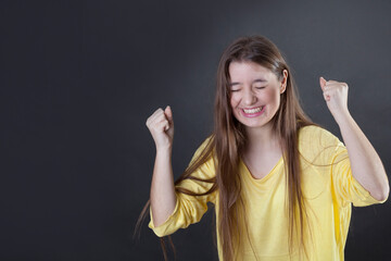 A cheerful young woman with her fists raised and her eyes closed.