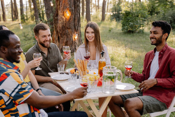 Meeting of multiracial group of friends toasting and drinking wine during party in the forest