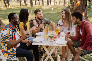 Meeting of multiracial group of friends eating dinner and drinking wine during party in the forest