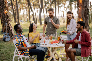 Meeting of multiracial group of friends eating dinner and drinking wine during party in the forest