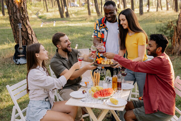 Meeting of multiracial group of friends eating dinner and drinking wine during party in the forest