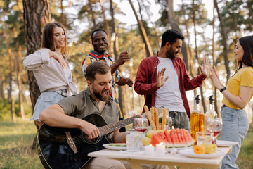 Multicultural group of people, bearded hipster man playing guitar and friends dancing and having fun
