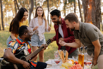 Multicultural group of people, African hipster man playing guitar and friends dancing, singing and having fun