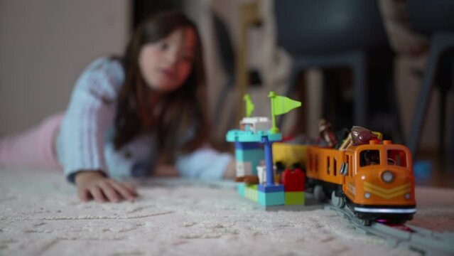 8-Year-Old Girl Playing with Toy Train on Home Floor, Engrossed in Railroad Play