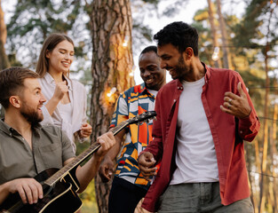 Multiracial group of people, bearded hipster man playing guitar and friends dancing, singing and having fun