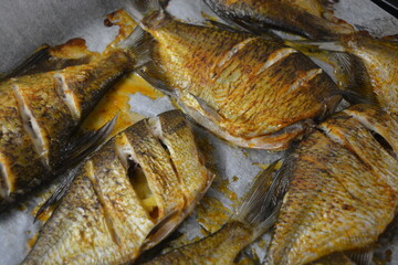 Delicious and healthy, baked fish, Carassius with lemon on a black baking sheet with white parchment paper.