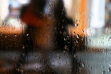 Abstraktes Motiv mit Regentropfenmuster vor Glasscheibe und zwei laufenden Frauen mit großen Taschen auf Gehweg vor Schaufenster mit Licht in der Stadt bei Regen und Sturm in der Nacht im Winter - obrazy, fototapety, plakaty
