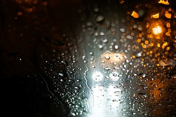 Abstraktes Motiv mit Regentropfenmuster vor Auto mit wei0en Lichtern auf Straße in der Nacht bei...