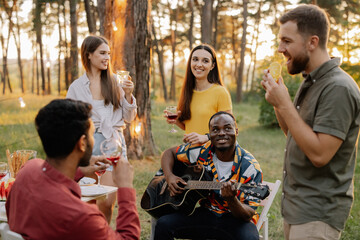 Multiracial group of friends, African man playing guitar around happy friends drinking wine
