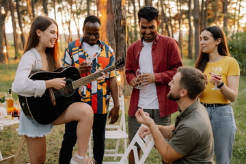 Attractive hipster woman playing guitar winning over men at dinner party with multiracial friends