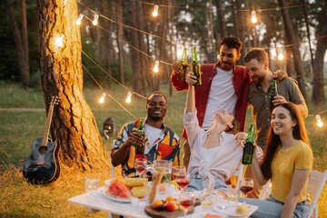 Group of multiracial friends having fun at party, drinking beer and making toast - obrazy, fototapety, plakaty