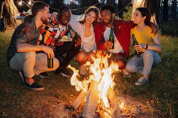 Multiracial friends sitting around the fire drinking beer and having fun at the party