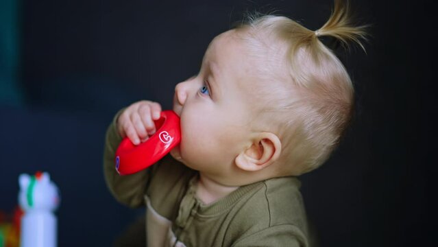 Beautiful baby with blond hair lies on his belly. Infant chews a red toy and lies down on his back. Close up.
