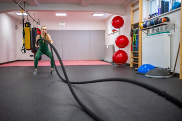 Young woman with perfect body doing crossfit exercises with a rope in the gym.