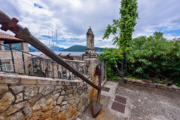 Herceg Novi, Montenegro - August 06, 2023: Ancient anchors and cannons stored in the Maritime Museum, an old bell tower and a stunning view of the Bay of Kotor behind it