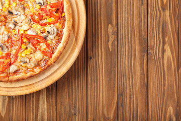 delicious pizza with chicken, mushrooms, cheese, tomatoes and corn on a wooden background