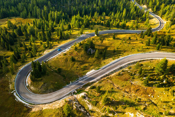 Car drives on curvy asphalt road winding along large forest with evergreen coniferous trees. Serpentine freeway across forestry mountains aerial view