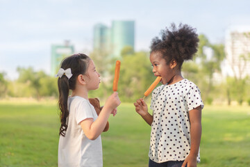 Happy cheerful white girls and black girl eat sausage together at outdoors park , Relationship...