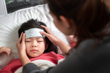Asian mother take cool gel for reduce high fever on sick girl forehead on bed at morning time, ...