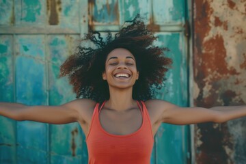 Fototapeta premium A carefree woman stands against a vibrant wall, her curly hair framing her closed eyes as she smiles in contentment