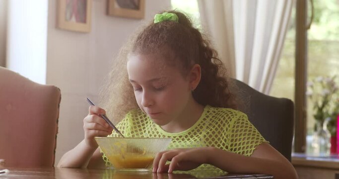 Pretty little girl with sitting at dining table in the home kitchen and eating pumpkin soup for breakfast. Balanced meal for child healthy growth concept.Child eating healthy organic vegan food. 4K