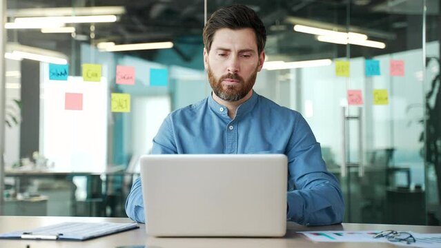 Thoughtful confident accountant works on laptop sitting at workplace in business office. Handsome financier in glasses is working on application on computer. Executive thinking about solving problems