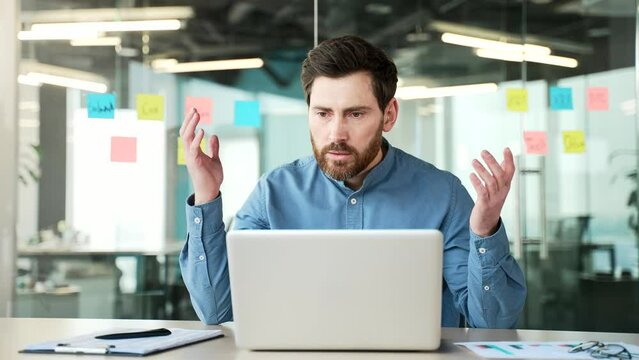 Shocked stressed businessman reads bad news on laptop while sitting at desk at workplace in business office. Frustrated worried worker is upset while reviewing negative information on a computer