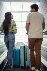 vertical portrait multicultural couple of travelers on airport escalator with luggage