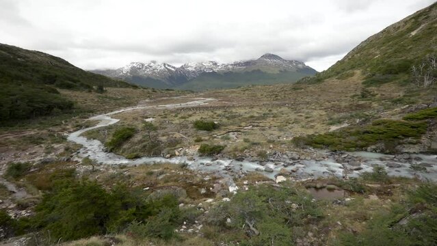 Alpine landscape in autumn. Panorama view of the glacier water stream flowing downhill across the yellow grassland, Andes mountains and forest in Ushuaia, Tierra del Fuego, Patagonia Argentina.