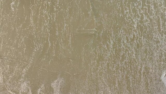 Aerial slow-motion over foamy waves splashing on a sandy beach on a sumer day