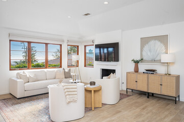 Spacious living room with hardwood floors, expansive windows, sleek white sofas, and coffee table